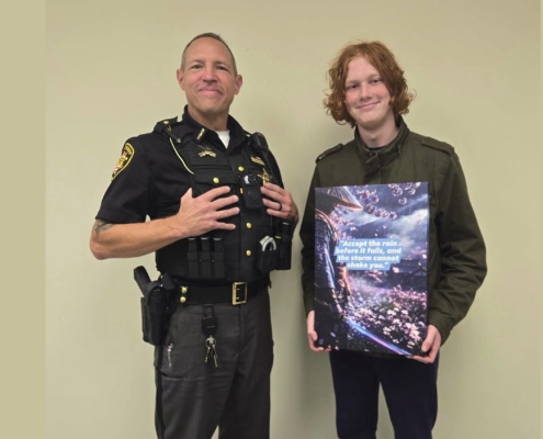 Fostoria News Police officer and young man holding a book together in an indoor setting.